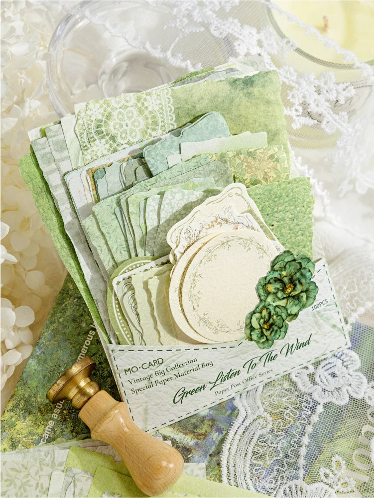 A stack of vintage green paper sheets and a wooden stamp are shown with lace fabric in the background.