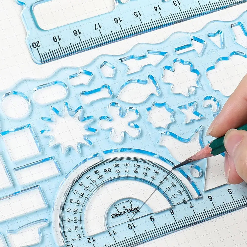 A hand uses a fine-tipped pen to draw on a clear plastic ruler set featuring various geometric shapes and measurement marking