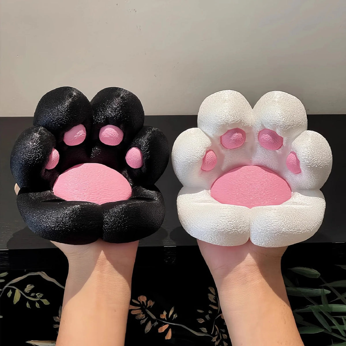 A pair of hands holds a black and pink 3D printed cat paw phone stand with an anti-slip base.