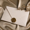 Beige Leinenbriefumschlag mit goldener Wachssiegel auf drapierter Satin-Stoff
