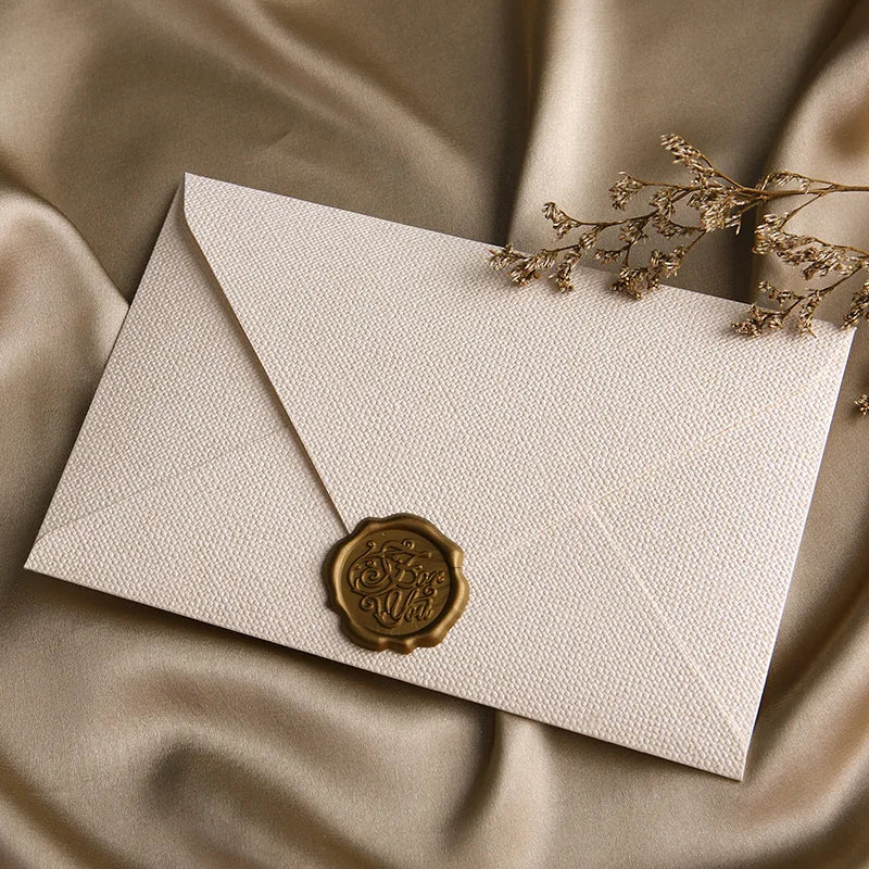 Beige Leinenbriefumschlag mit goldener Wachssiegel auf drapierter Satin-Stoff
