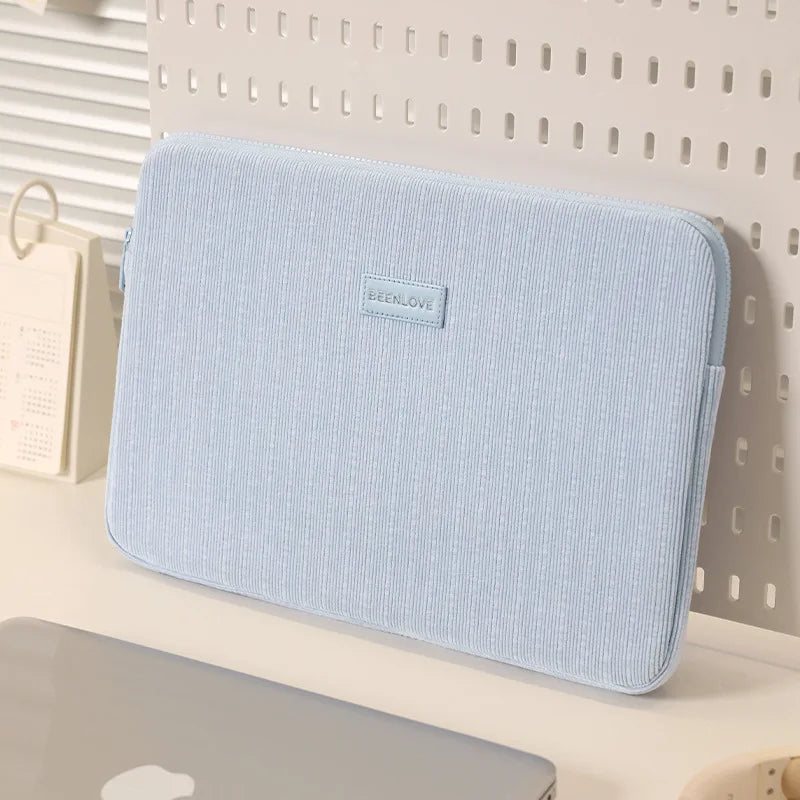 A light blue fabric laptop sleeve is displayed on a white surface next to a white grid background.
