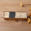 A wooden stamp seal set with numbered and alphabetical characters is displayed on a wooden surface next to dried flowers.