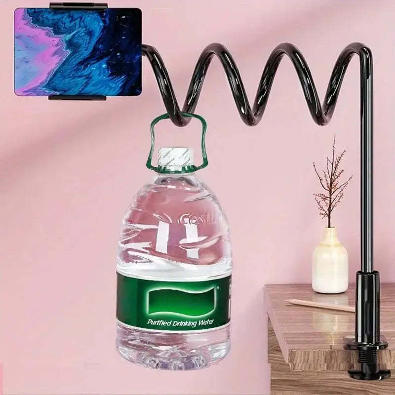 A clear glass bottle of drinking water is suspended by a gooseneck tablet holder against a pink wall.