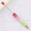 A DIY beadable pen set with a pink and yellow gradient barrel and a magenta tip resting on a white tiled surface.
