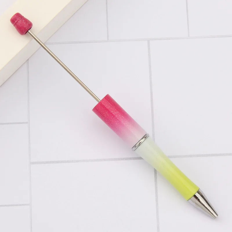 A DIY beadable pen set with a pink and yellow gradient barrel and a magenta tip resting on a white tiled surface.