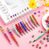 A collection of colorful plastic beaded ballpoint pens in various shades and designs arranged on a pink background.