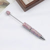 A silver pen accessory with a rhinestone-encrusted tip and a decorative, sparkly top, displayed on a white surface.