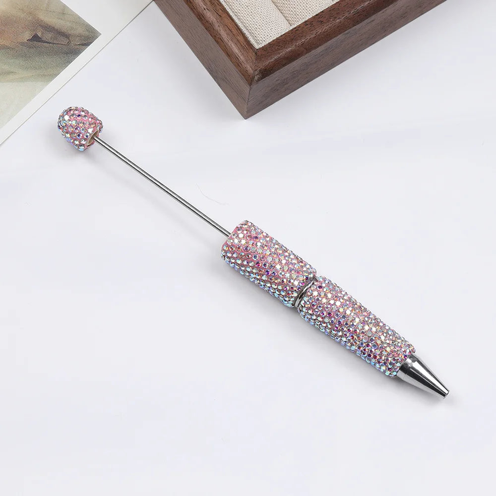 A silver pen accessory with a rhinestone-encrusted tip and a decorative, sparkly top, displayed on a white surface.
