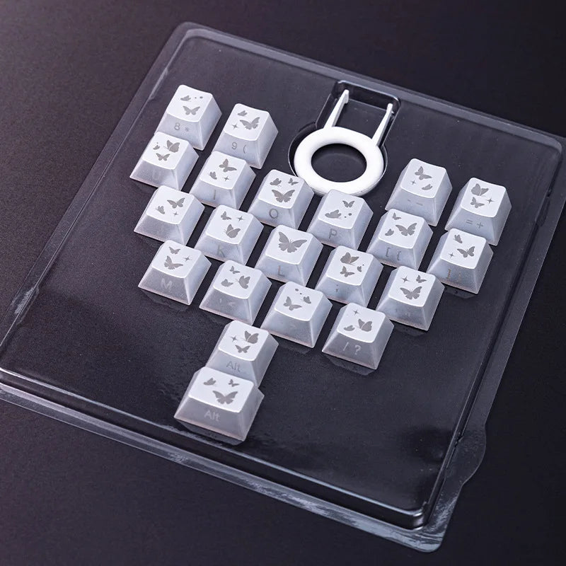 Klare Kunststoffschale mit weißen Butterfly-Keycaps und einem Keycap-Puller-Werkzeug für mechanische Tastaturen