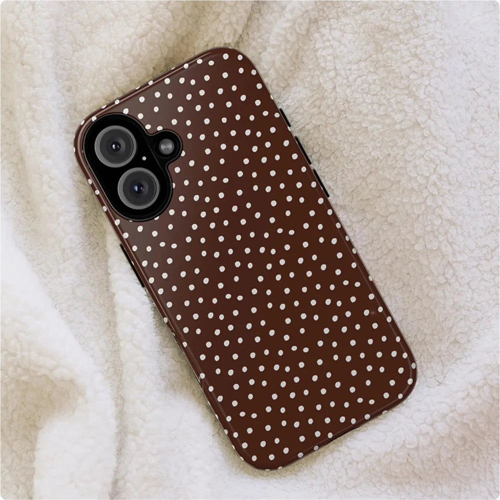 A brown phone case with white polka dots resting on a fluffy beige fabric.