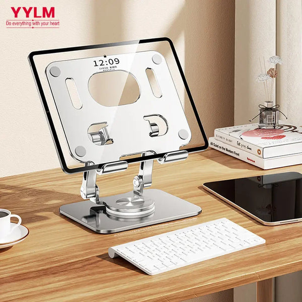 A clear acrylic tablet stand with a rotating mechanism is shown on a wooden desk next to a laptop and keyboard.