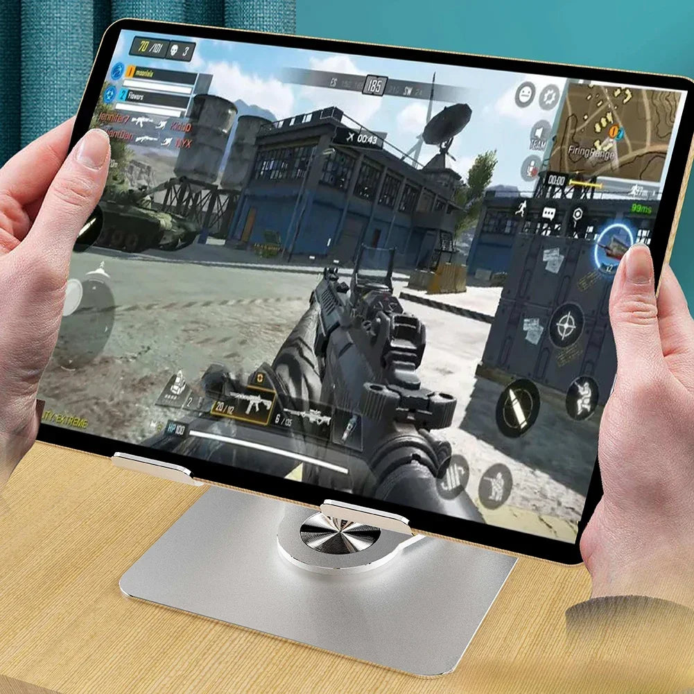 A hand holds a foldable tablet displaying a first-person shooter game, resting on a silver stand.