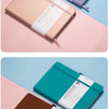 Two notebooks in purple and brown leather are displayed on a pink surface.