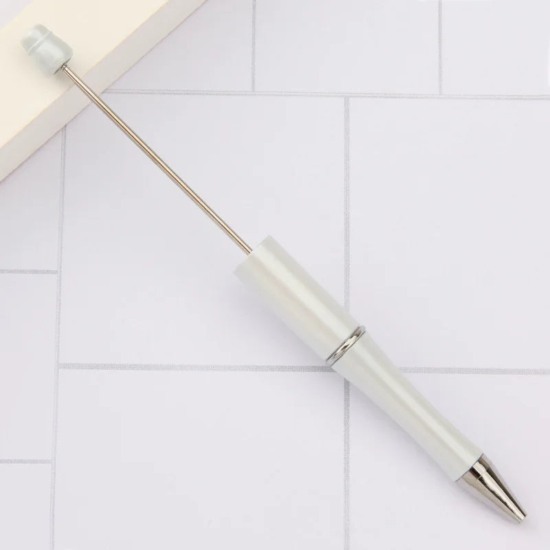 A silver and white DIY beadable pen set with a black ink tip resting on a white tiled surface.