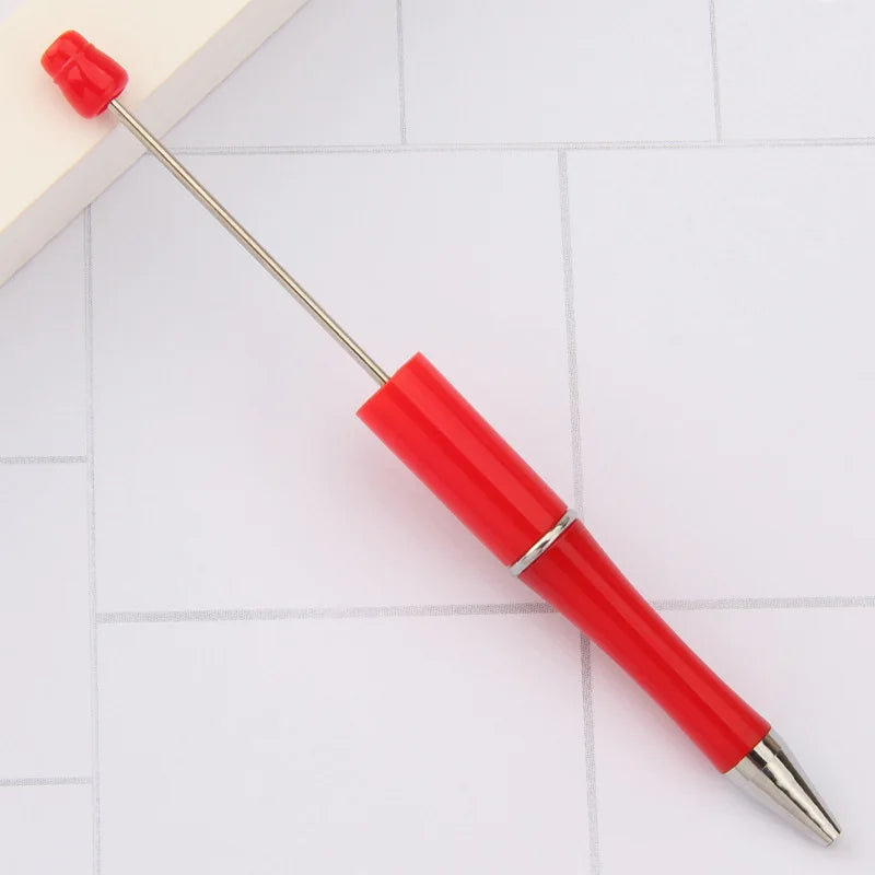 A red DIY beadable pen with a silver tip and a red cap resting on a white surface.