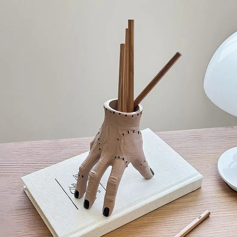 A hand-shaped decoration made of spooky resin palm leaves with wooden sticks, resting on a white book.