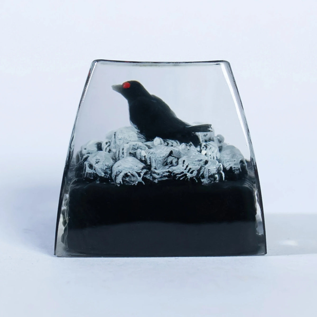 A resin keycap featuring a black raven perched atop a skull, set in a clear glass-like mold.