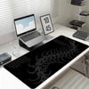 Black gaming mouse pad featuring a white gothic centipede design placed on a white desk next to a laptop.