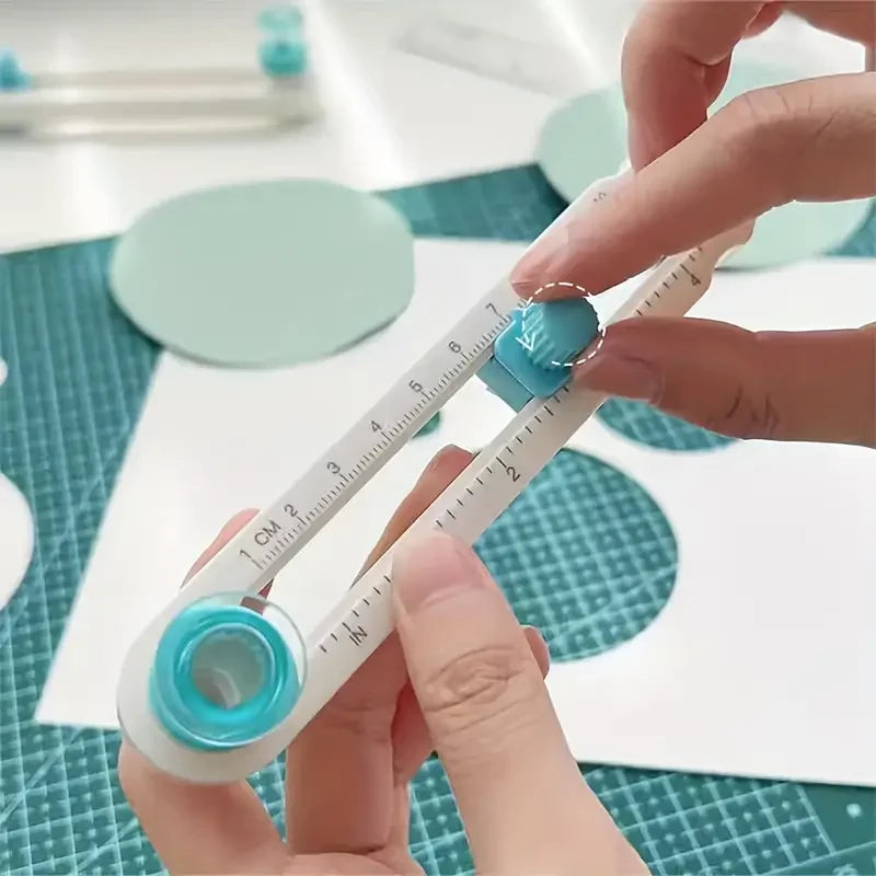 A hand is using a white and blue adjustable circle cutting tool to measure or cut on a green grid surface.