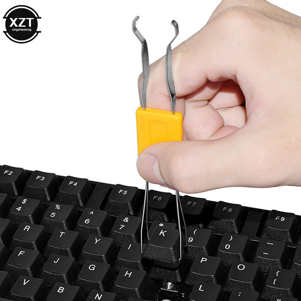 A hand is using a stainless steel keycap and switch puller tool to remove a keycap from a mechanical keyboard.
