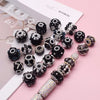 A collection of black and silver acrylic flower beads for jewelry making displayed on a pink background.