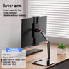 A black adjustable monitor stand with a lever arm is shown on a wooden desk.