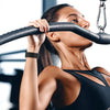 A woman grips a black exercise bar with a black elastic band, exercising in a gym setting.