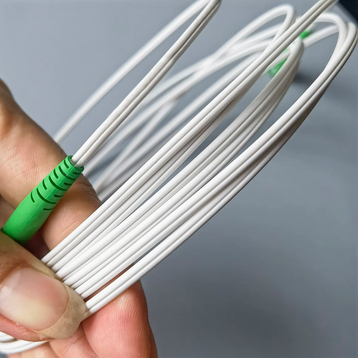 A hand is holding a bundle of white fiber optic cables with green connectors.