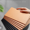 A stack of simple cowhide suture notebooks in shades of tan and black are displayed on a gray surface.