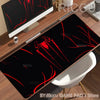 A black desk mat featuring a red spider-man design placed on a wooden desk next to a computer monitor.