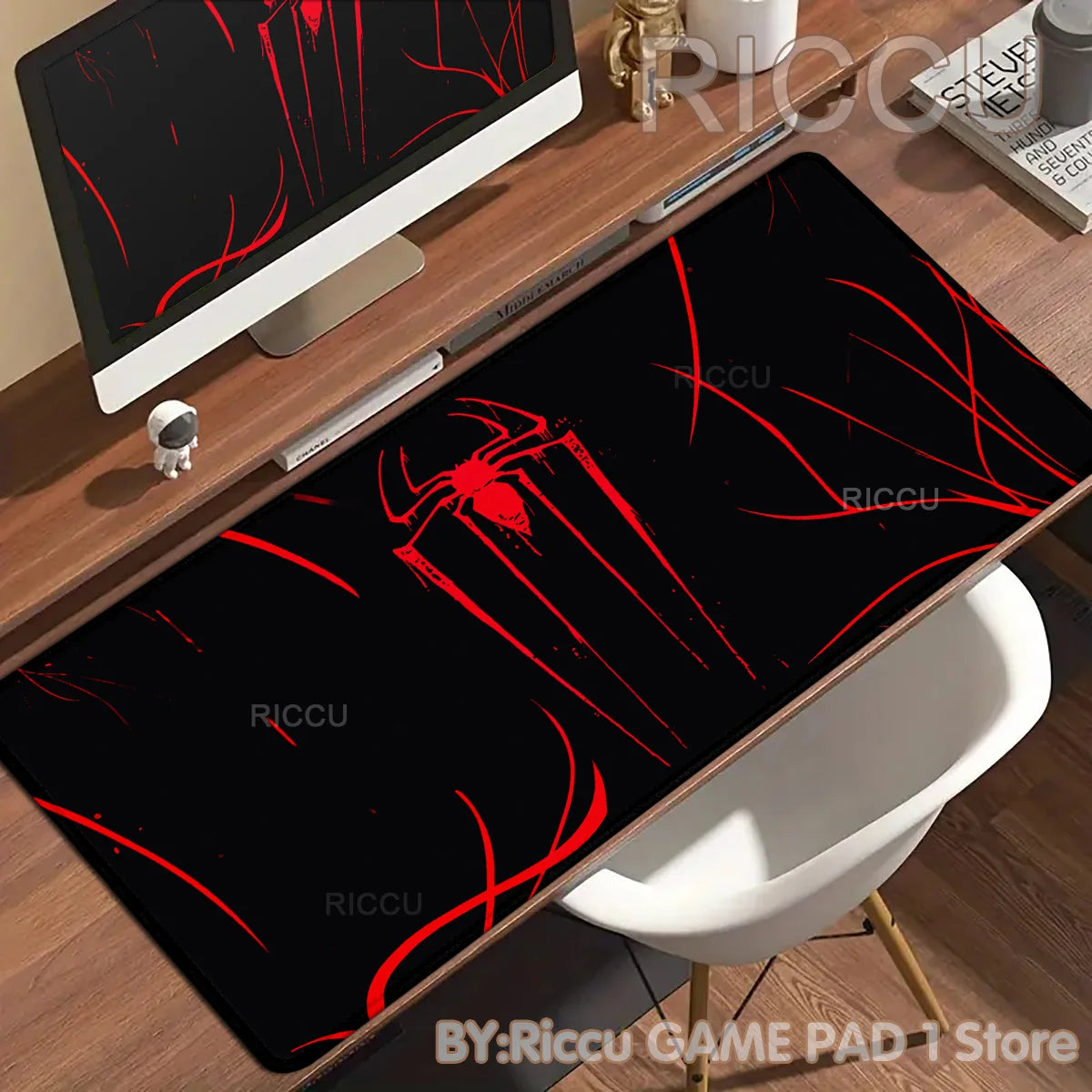 A black desk mat featuring a red spider-man design placed on a wooden desk next to a computer monitor.