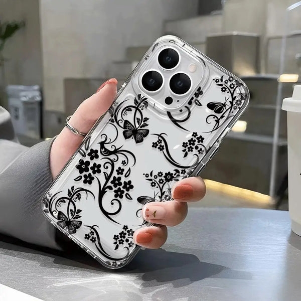A hand holds a clear phone case with a black floral pattern featuring butterflies and vines against a white background.