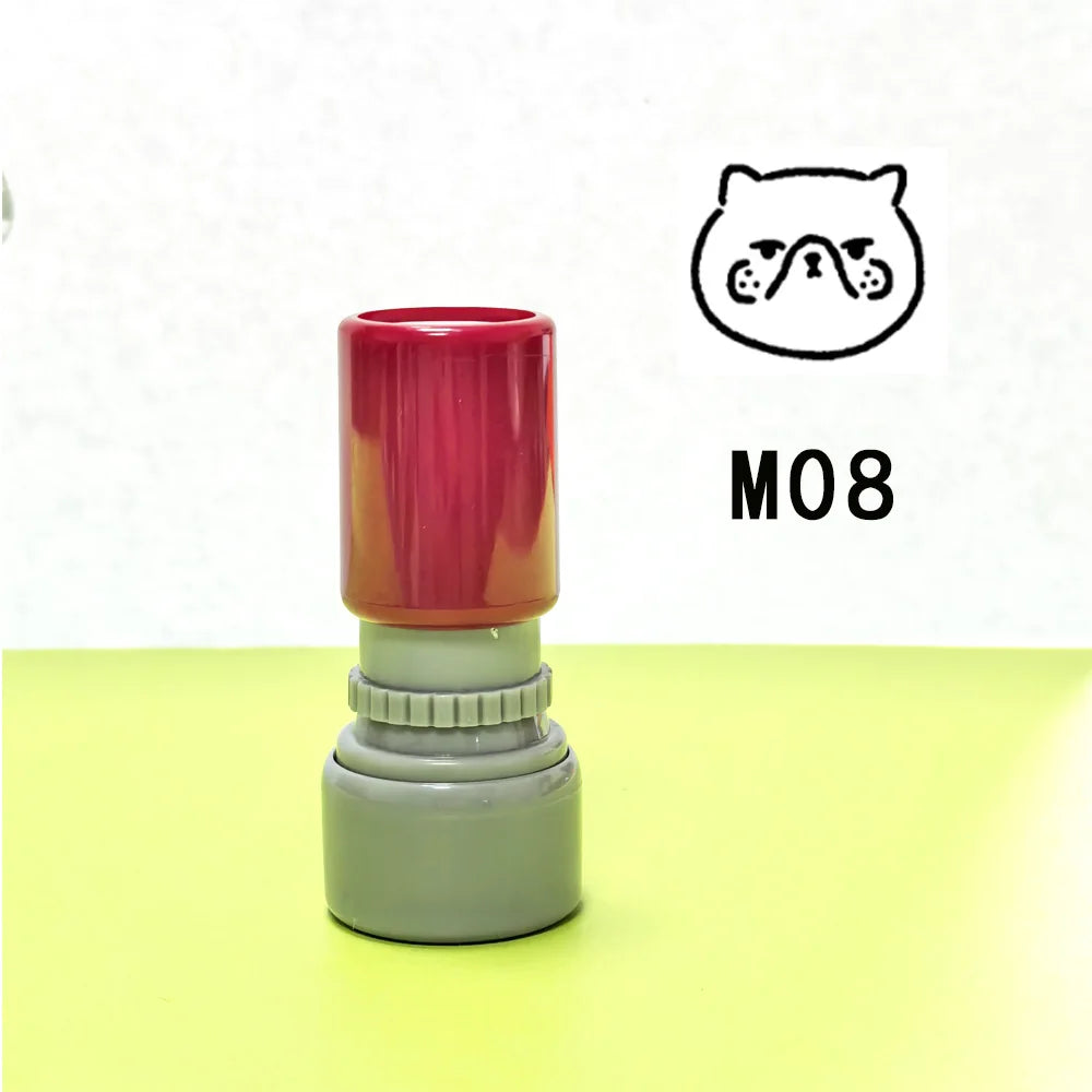 A red and gray teacher stamp with a cat face design is shown on a yellow surface.