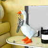 A white ceramic duck figurine with an orange beak holding a set of metal keys, displayed on a glass table.