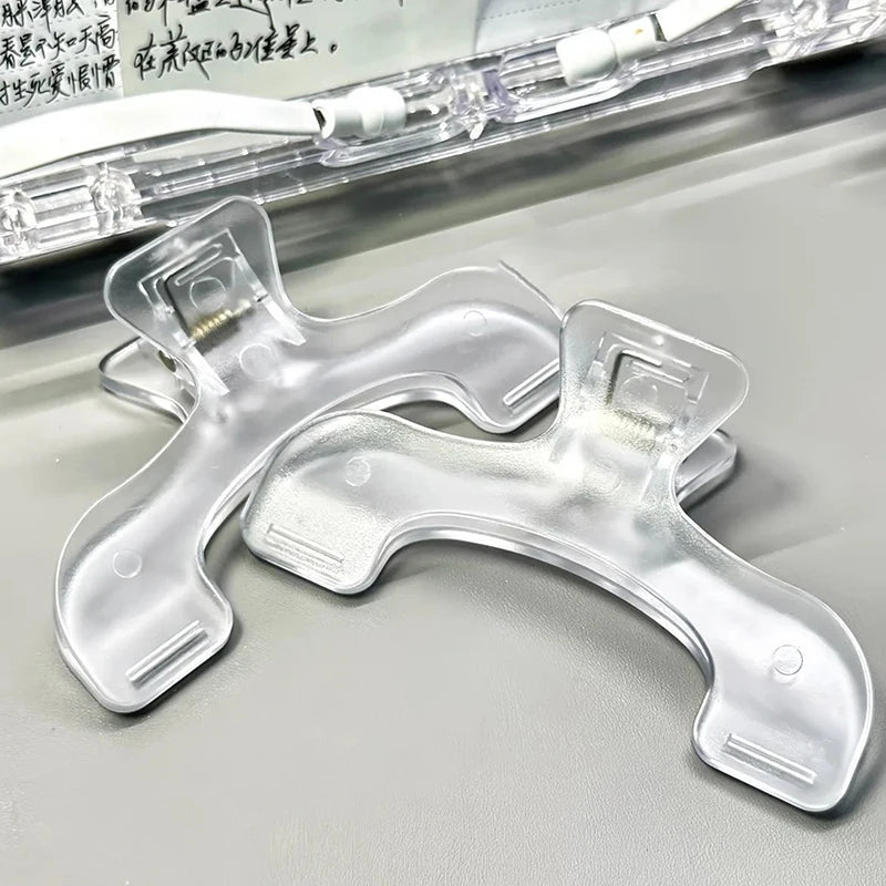 Clear plastic book page clips with a light frosted finish shown on a gray surface.