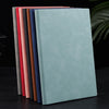 A stack of premium A5 leather journals in various muted colors, including red, pink, brown, and blue, displayed on a dark sur