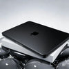 A black Apple laptop is shown inside a white protective case, resting on a reflective surface.