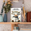 A monthly planner cover featuring a cute white bull with horns and a floral wreath, displayed on a wooden shelf.