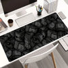 A black desk mat featuring a pattern of rolled-up paper scrolls on a white desk.