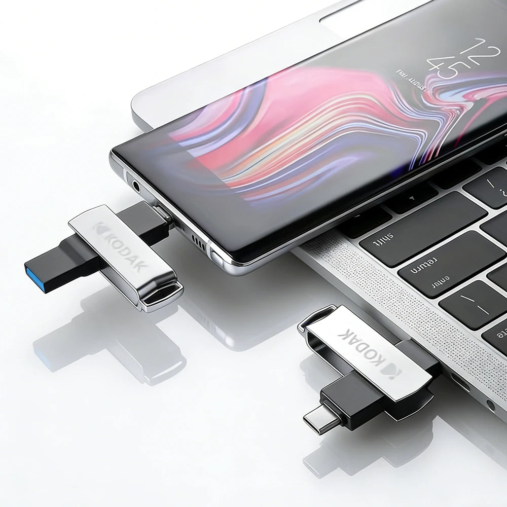 A black smartphone and a metal USB flash drive are shown on a white surface.
