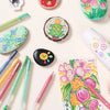A collection of acrylic paint markers in various colors and tips, including a round painted item and a colorful floral art sh