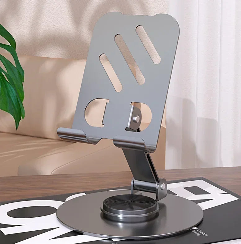 A silver 360-degree rotating mobile phone holder mounted on a stand, shown in a home setting.