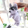 A hand is holding a white and gray plush dog toy against a window background.