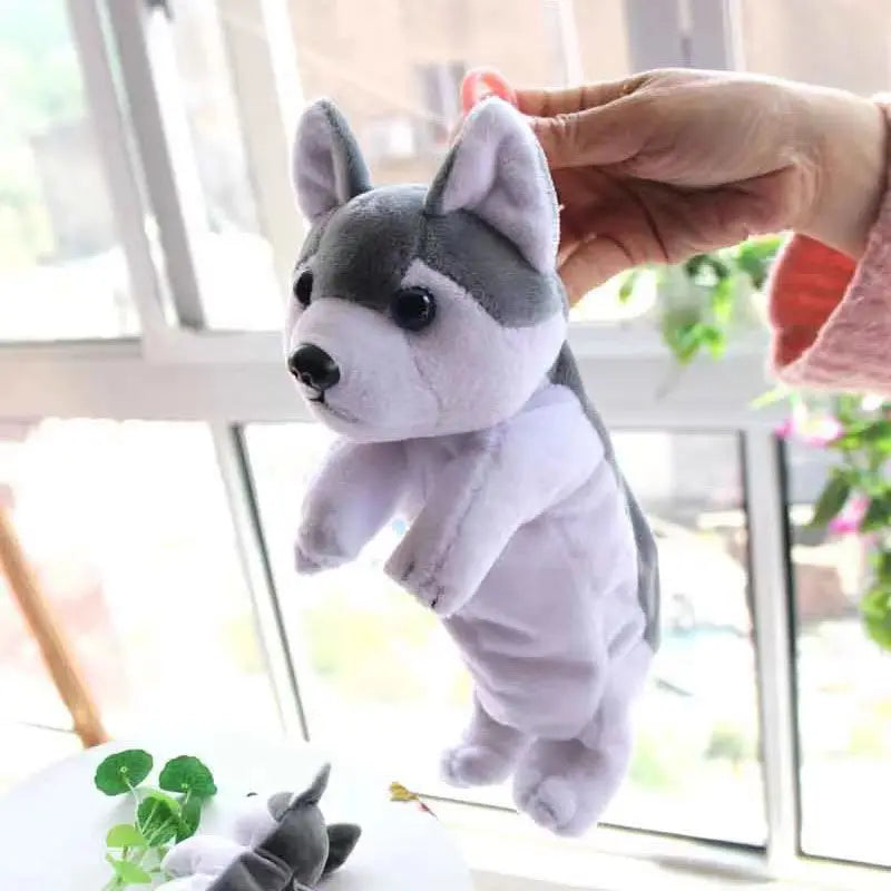 A hand is holding a white and gray plush dog toy against a window background.
