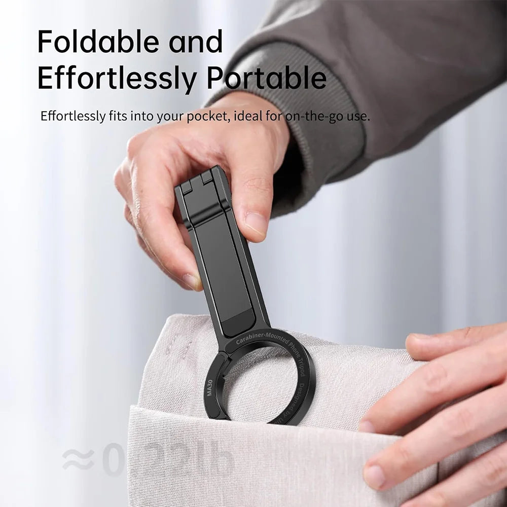 A hand is holding a black magnetic phone tripod stand with a carabiner attached, demonstrating its portable design.