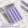 A clear plastic mini calculator with purple buttons and a digital display is shown on a sheet of paper.