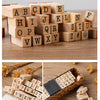 A collection of wooden alphabet stamp seals arranged in rows on a wooden surface.
