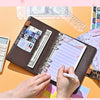 A hand is writing in a brown leopard print A6 binder with a clear plastic cover and loose leaf sheets on an orange surface.