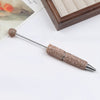 A long, silver pen accessory with a gold rhinestone ball and a textured beaded tip resting on a white surface.